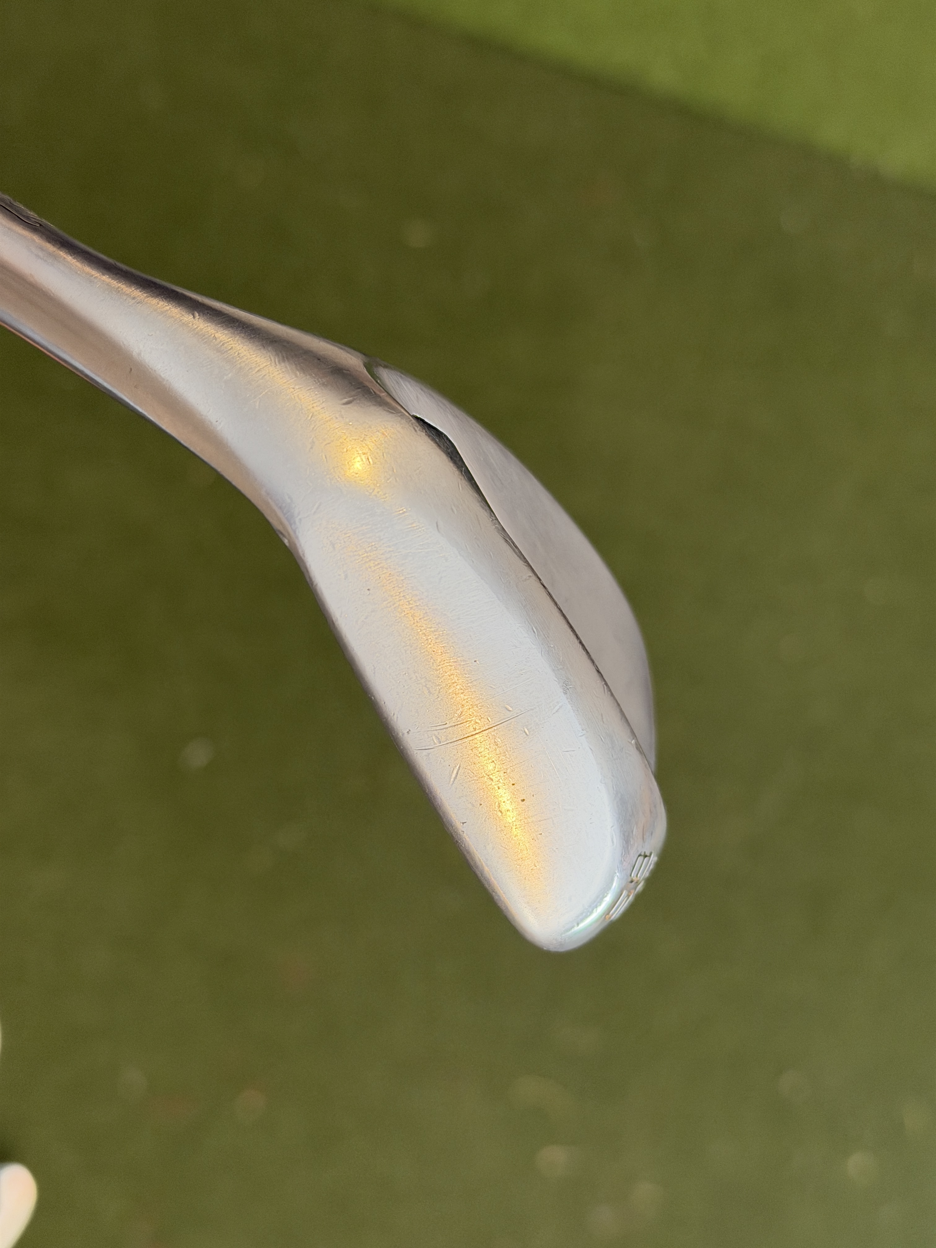 Close-up of a golf putter with white/cream colored head against a soft green background