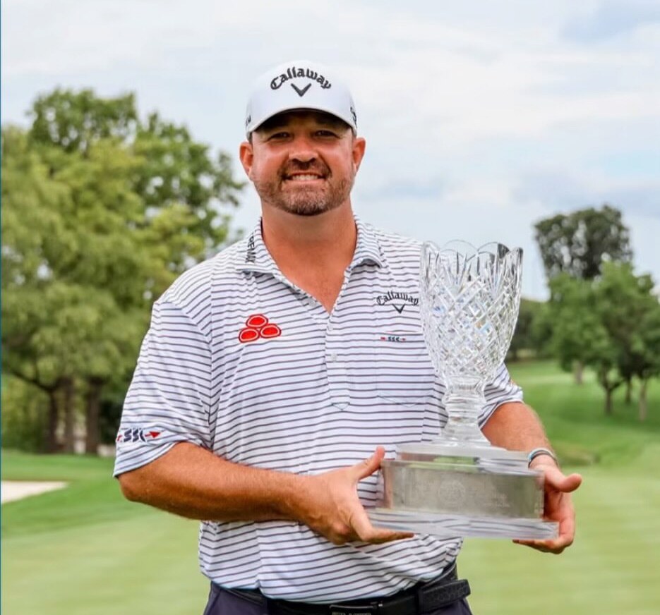 Brandon Holtz smiling and holding a crystal trophy on a golf course