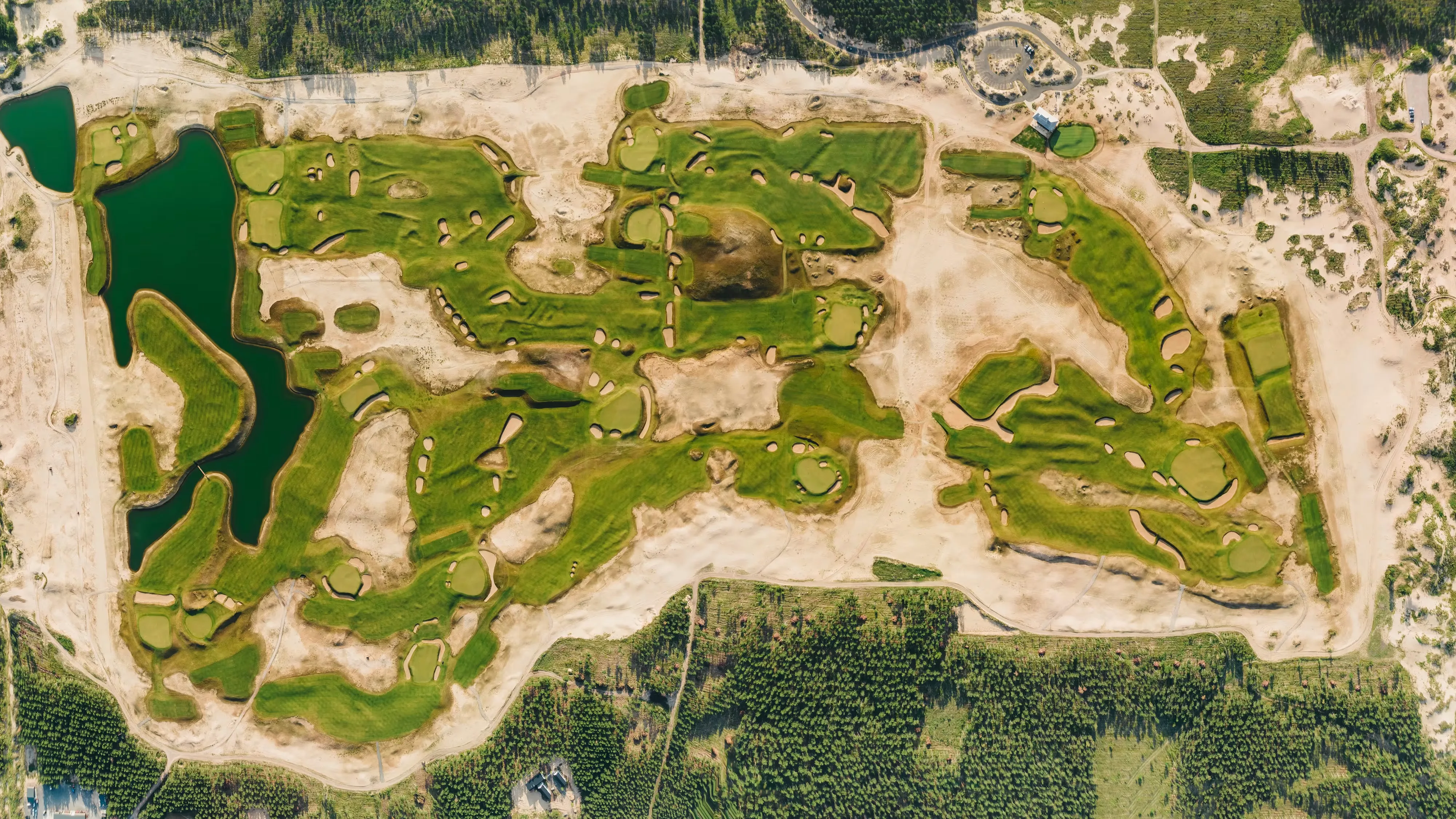 Overhead view of a golf course with green fairways, sand bunkers, water features, and surrounding forest.